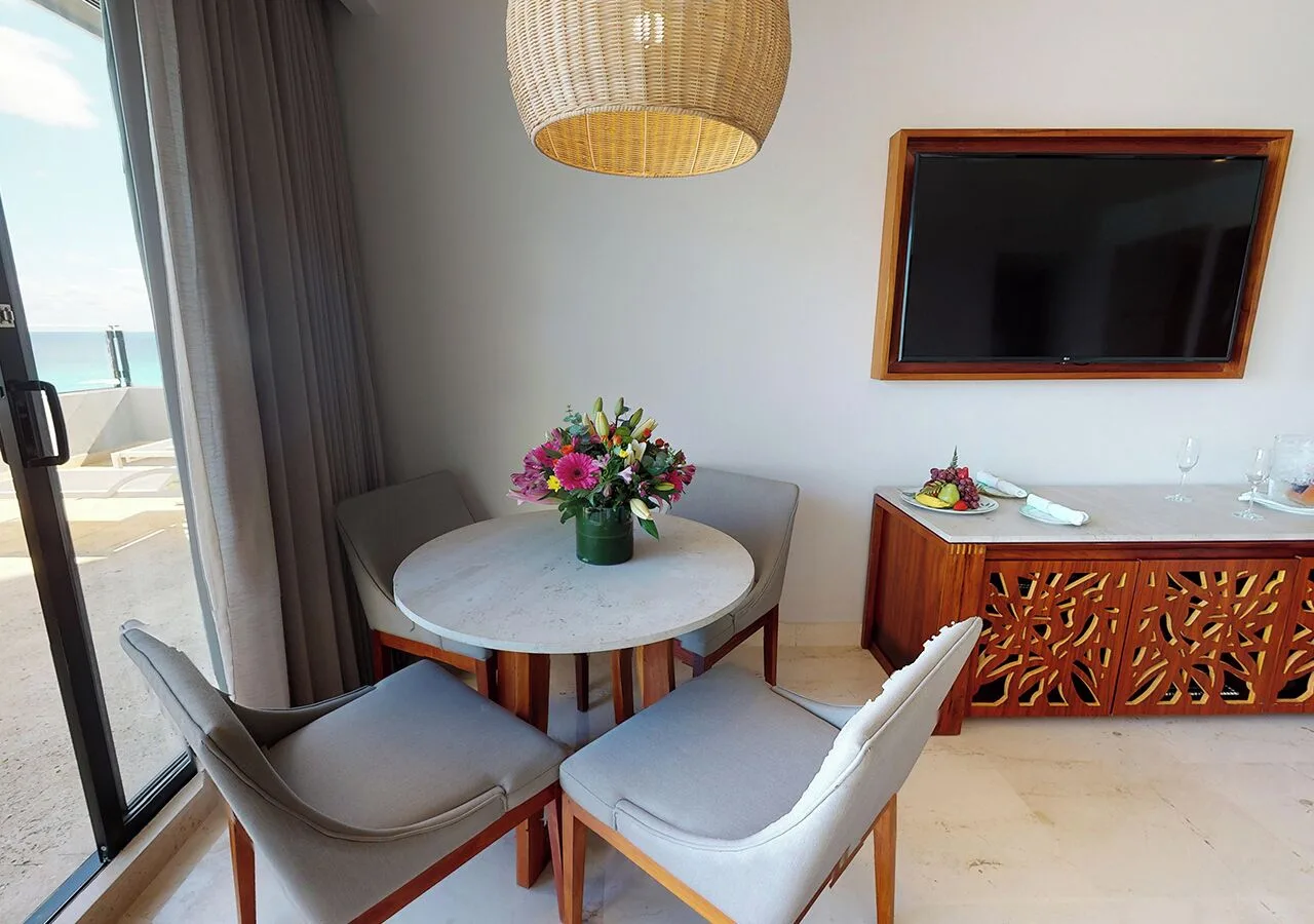 Round dining table, TV, and balcony door in a suite at Park Royal Beach Cancun.
