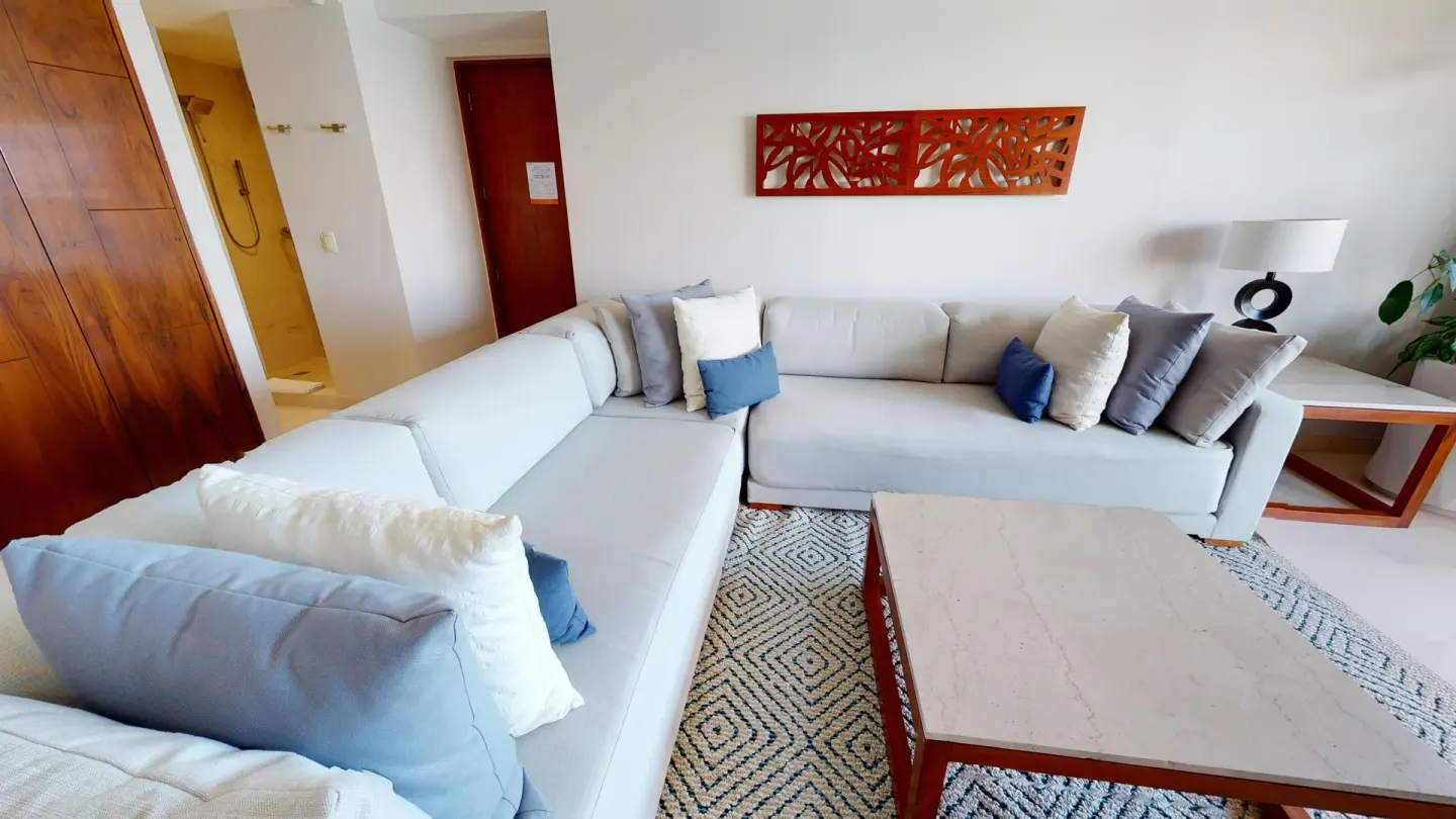 Sectional sofa, coffee table, and open shower area in a suite at Park Royal Beach Cancun.