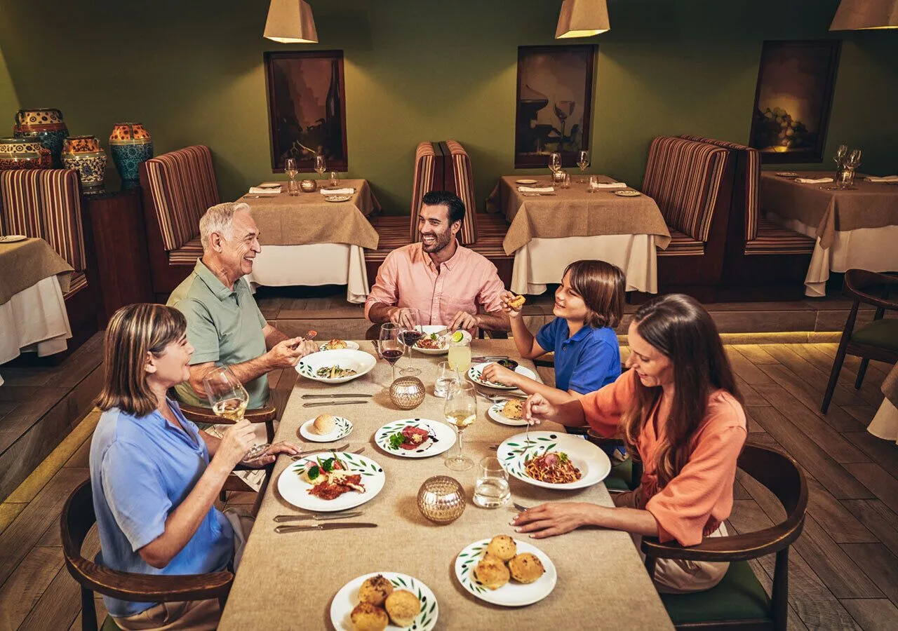 Family dinner in a warm restaurant at Park Royal Beach Cancun with booth seating behind them.