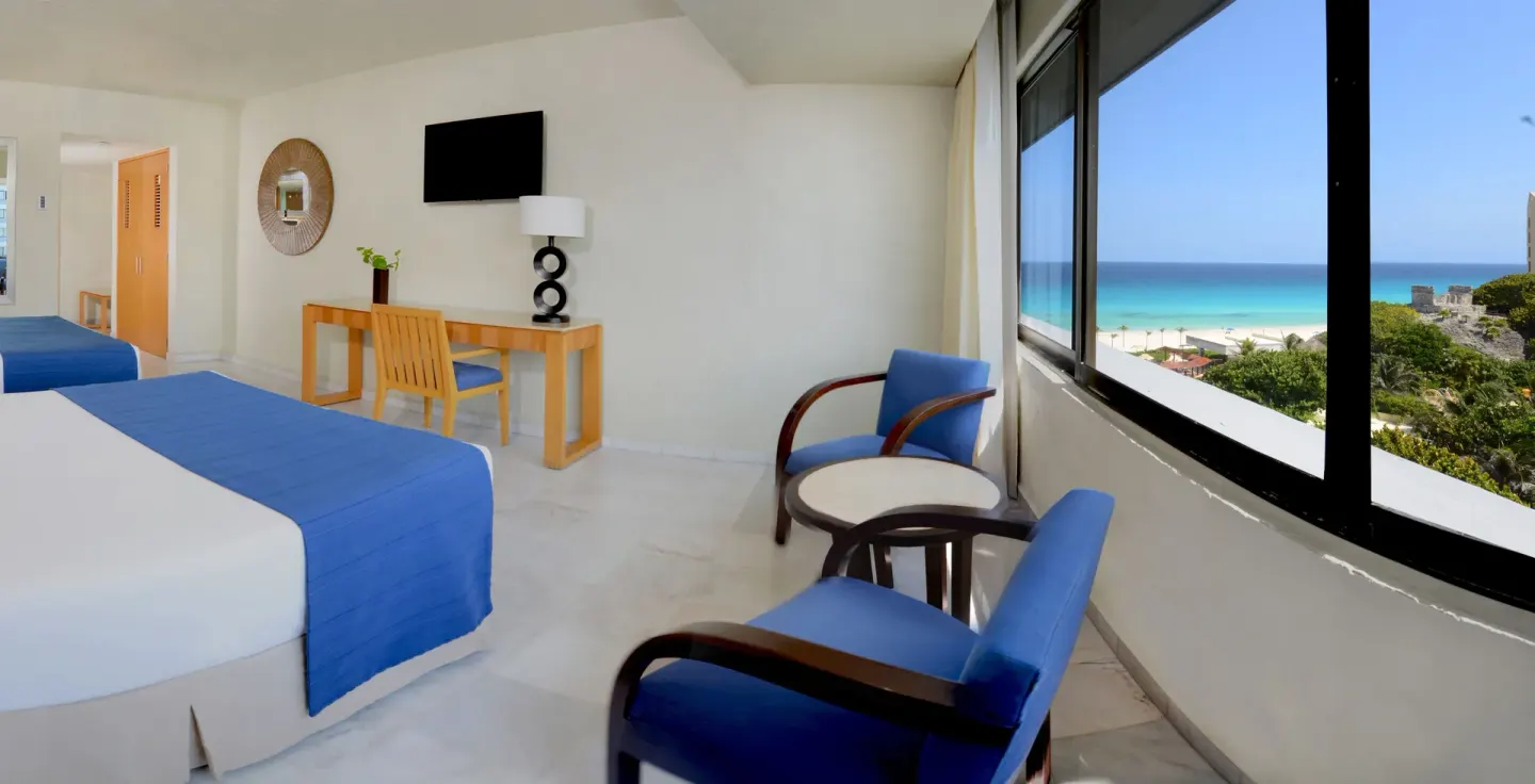 Deluxe ocean view room with two beds, seating and large windows at Park Royal Beach Cancun.