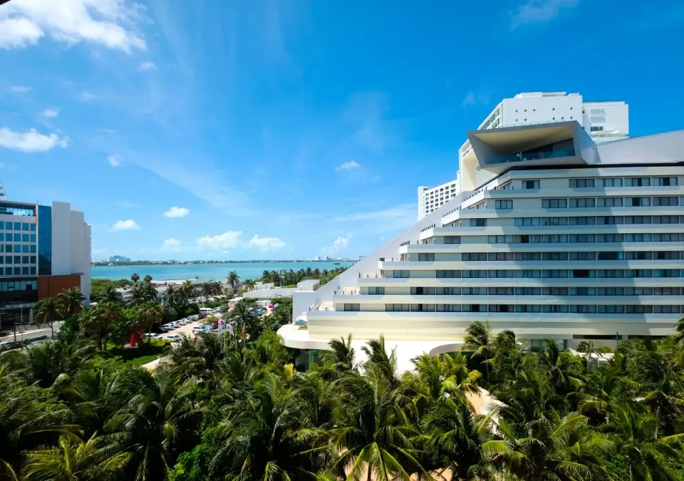 Family Suite balcony view at Park Royal Beach Cancun overlooking palms, nearby buildings, and blue lagoon water.