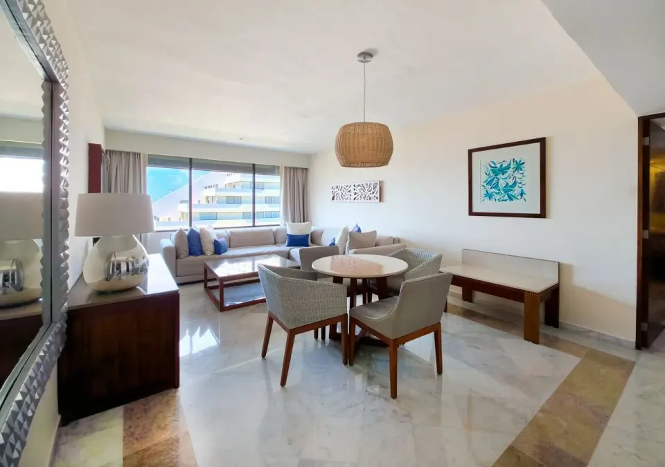 Family Suite living and dining area at Park Royal Beach Cancun with sofas, round table, and large window.