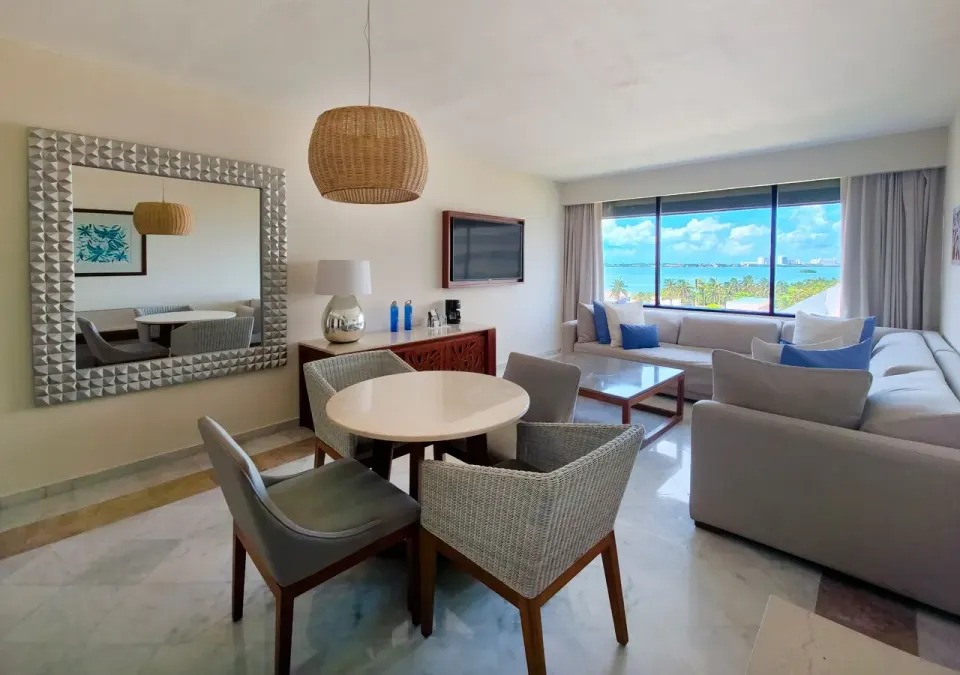 Family Suite lounge at Park Royal Beach Cancun with dining table, sofa, wall TV, and lagoon-facing window.