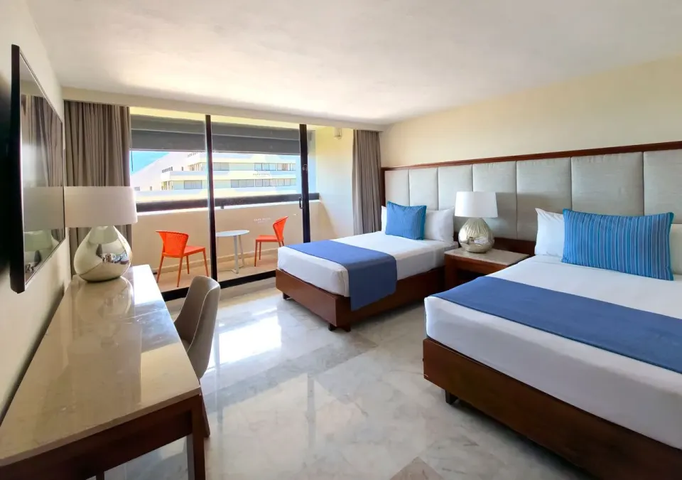 Family Suite two-bed room at Park Royal Beach Cancun with padded headboard and balcony seating outside.