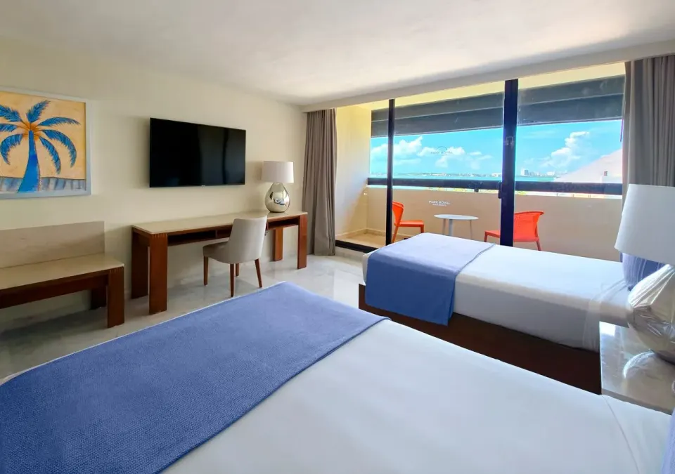 Family Suite bedroom at Park Royal Beach Cancun with two beds, TV, desk, and balcony view.