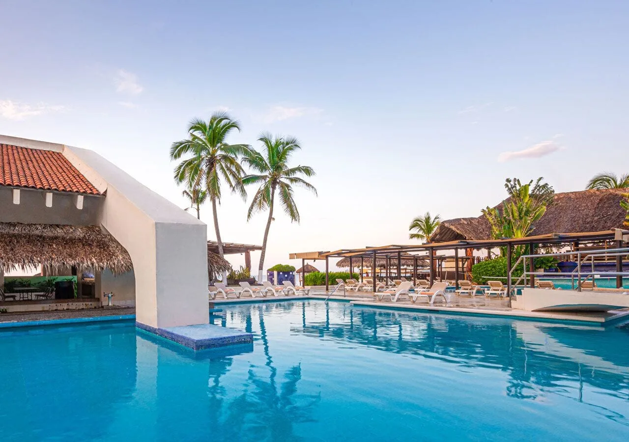 Pool deck with palapas, lounge chairs, and palms at Park Royal Beach Ixtapa.