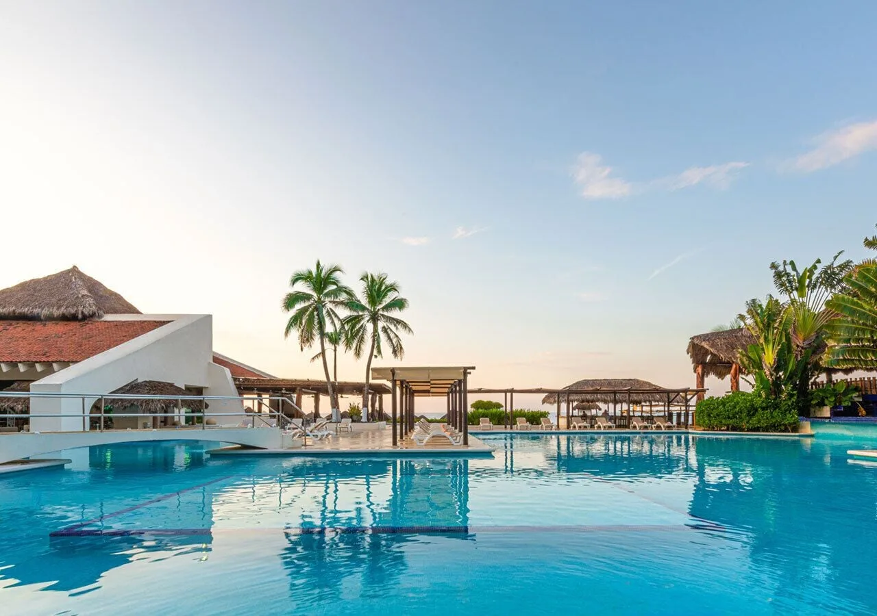 Pool with lounge chairs, palms, and ocean beyond at Park Royal Beach Ixtapa.
