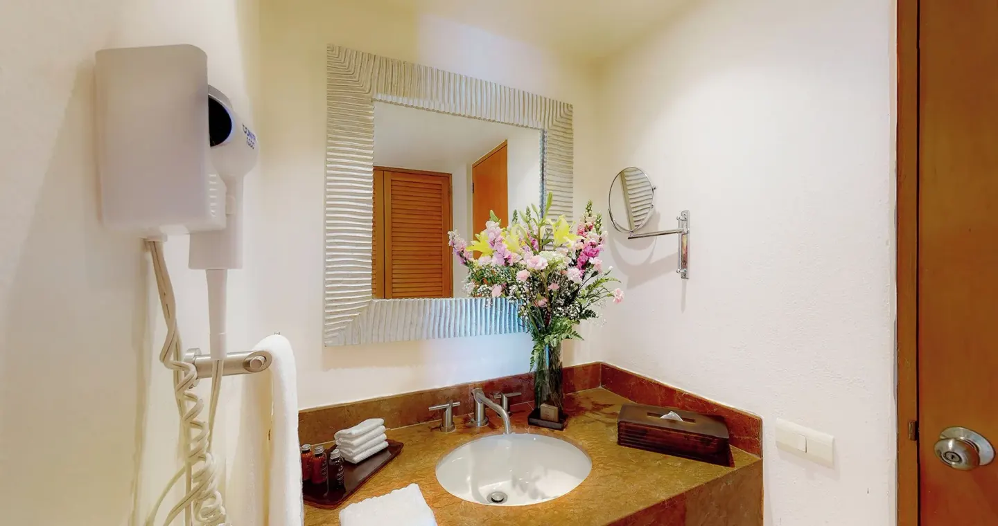 Master Suite bathroom vanity at Park Royal Beach Ixtapa with sink, mirror, flowers, and wall hair dryer.