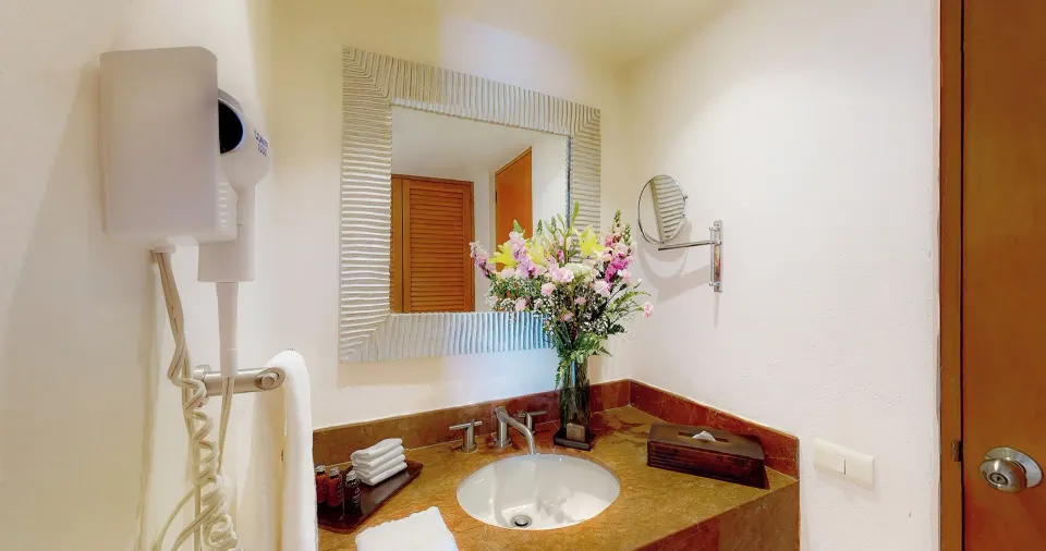 Master Suite bathroom vanity at Park Royal Beach Ixtapa with sink, mirror, flowers, and wall hair dryer.