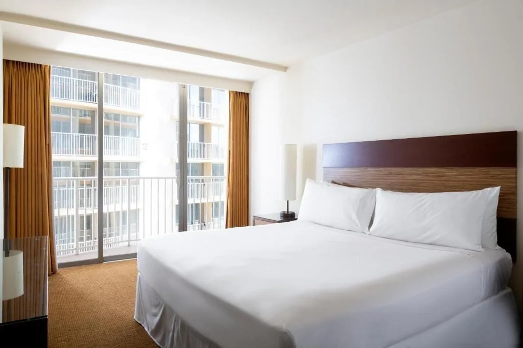 Standard Room king bed beside balcony doors overlooking nearby building balconies at Park Shore Waikiki.