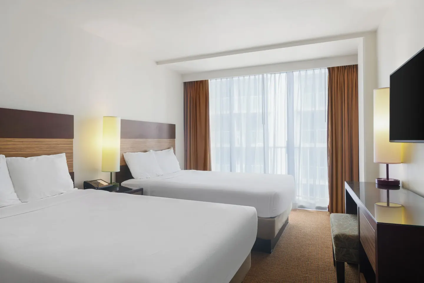Standard Room with two beds, TV, desk, lamps, and balcony curtains at Park Shore Waikiki.