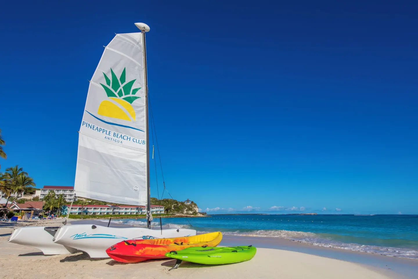 Kayaks and a sailboat rest on the beach at Pineapple Beach Club Antigua.