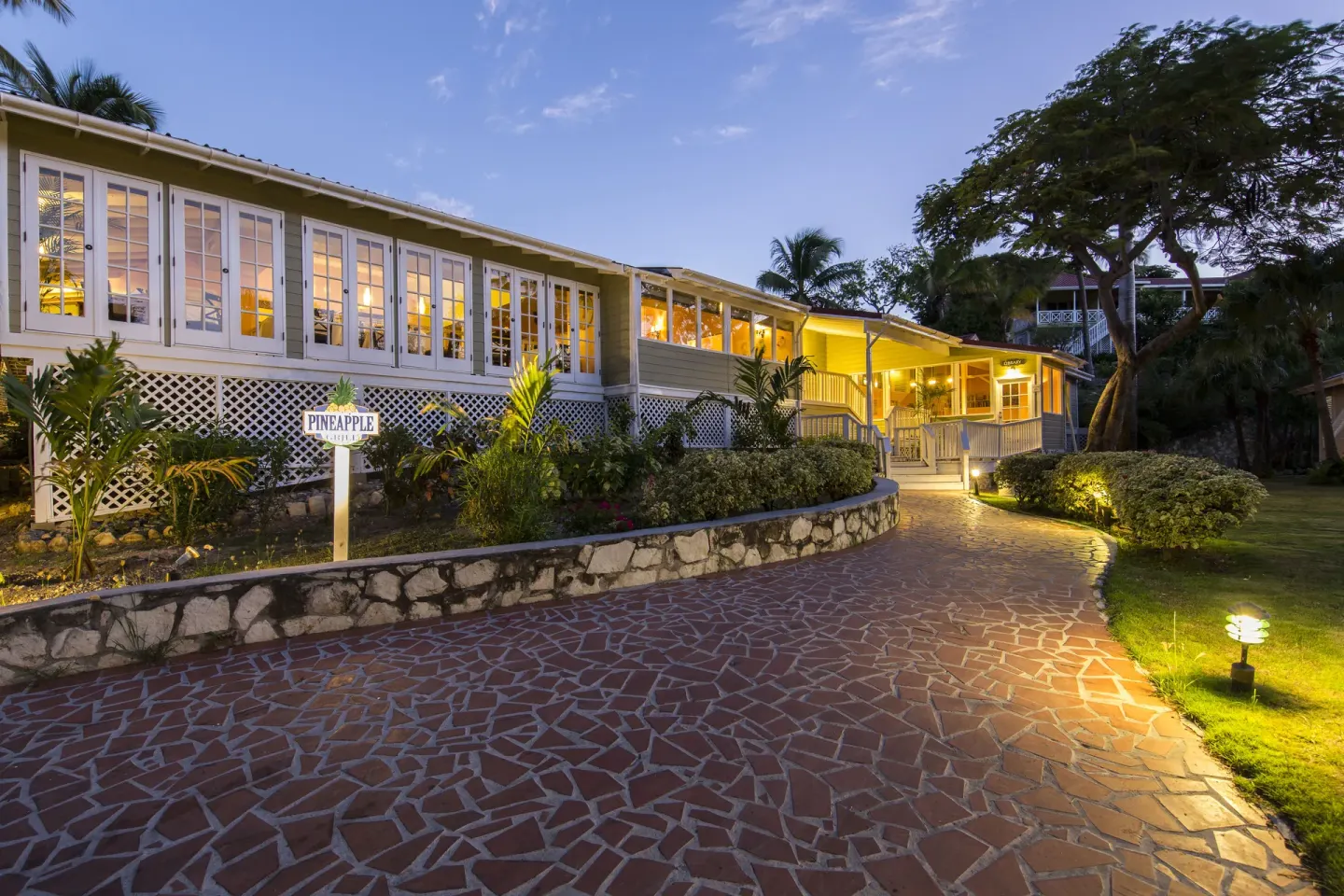 Evening walkway beside a lit restaurant building at Pineapple Beach Club Antigua.
