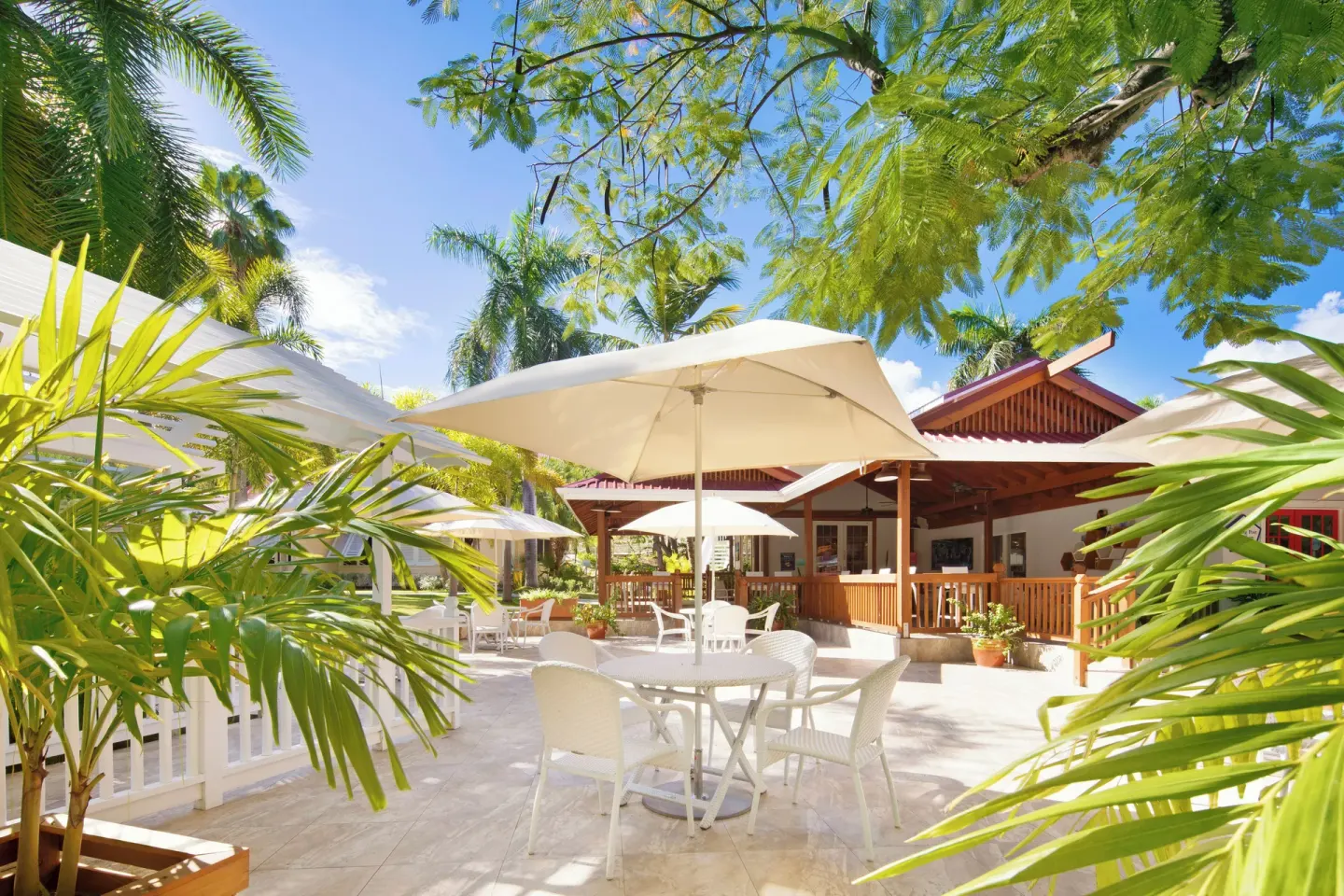 Umbrella-shaded patio seating surrounded by tropical plants at Pineapple Beach Club Antigua.
