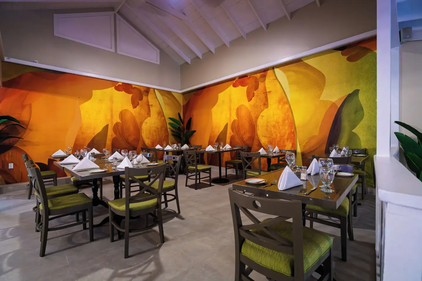 Dining room with orange floral mural and set tables at Pineapple Beach Club Antigua.