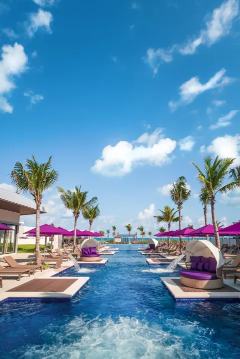 Long resort pool lined with palm trees and purple cabanas at Planet Hollywood Cancun.