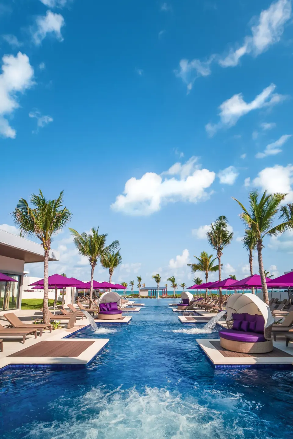 Long resort pool lined with palm trees and purple cabanas at Planet Hollywood Cancun.