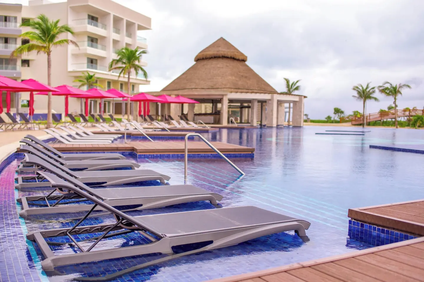 In-pool lounge chairs facing a thatched-roof pool bar at Planet Hollywood Cancun.