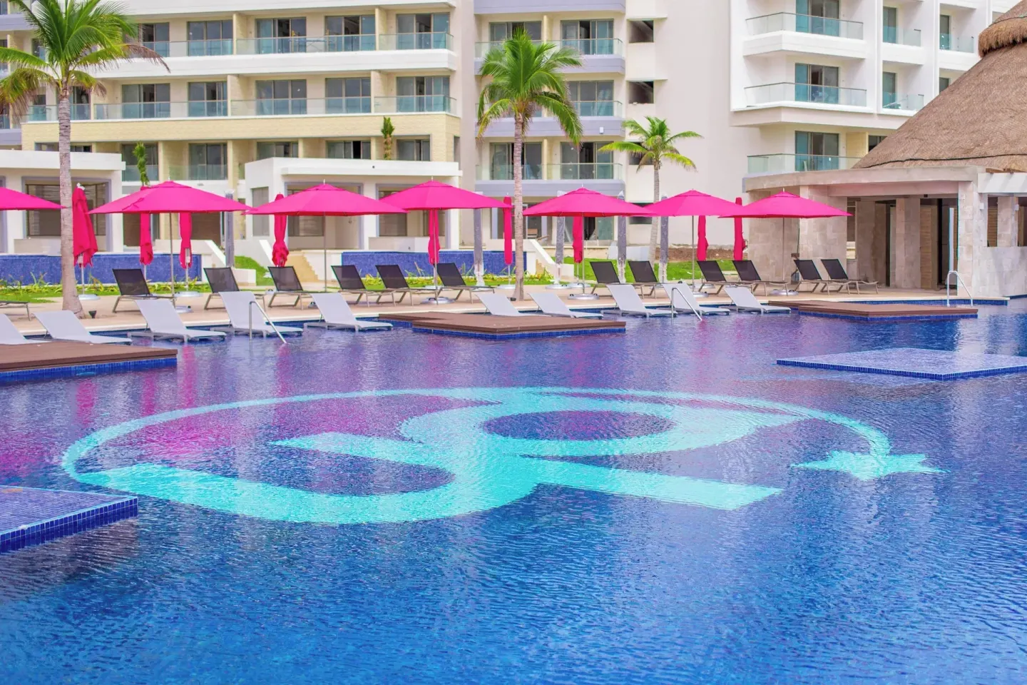Large resort pool with a turquoise emblem and pink umbrellas at Planet Hollywood Cancun.