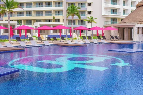 Large resort pool with a turquoise emblem and pink umbrellas at Planet Hollywood Cancun.