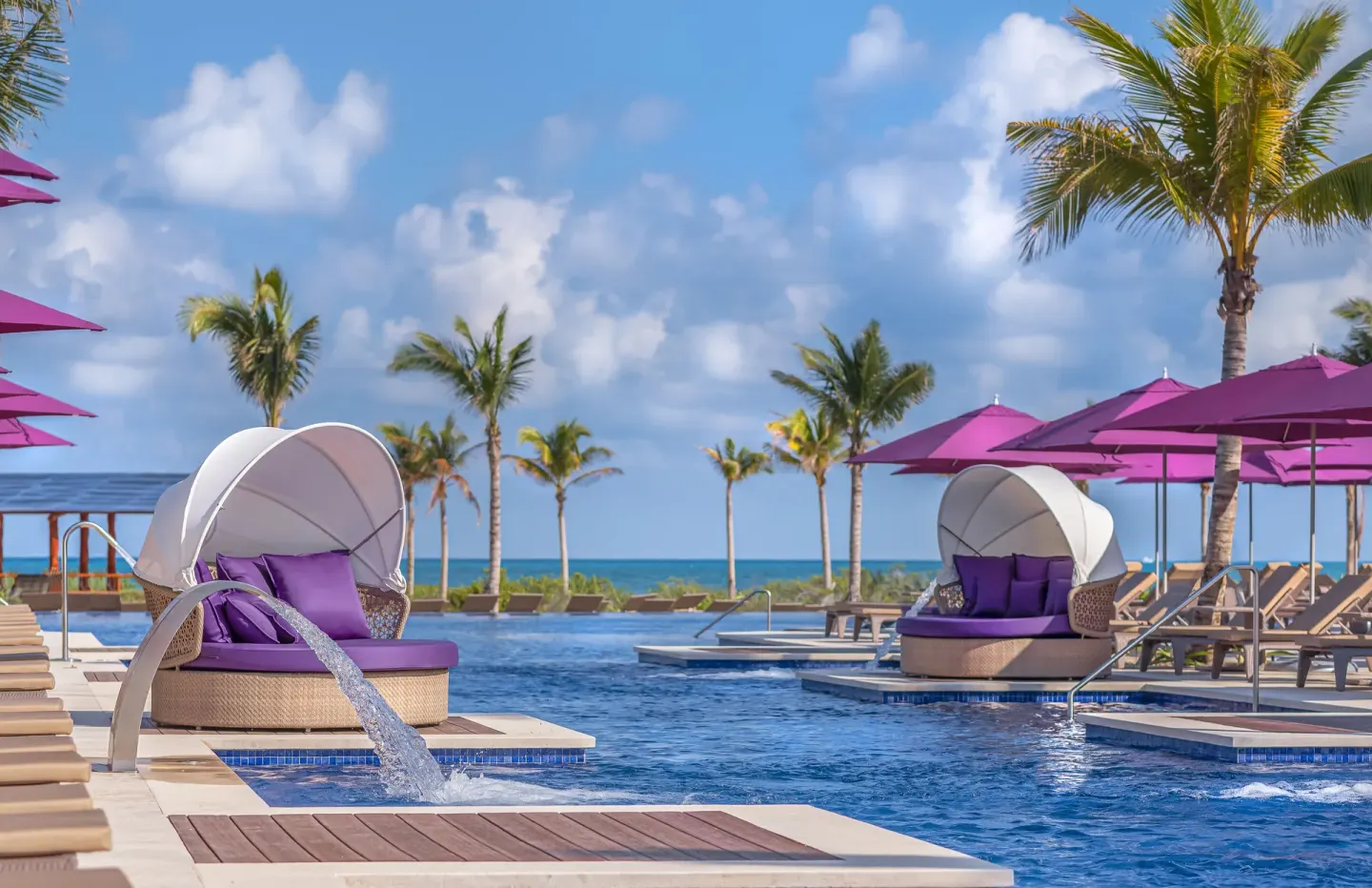 Pool with purple umbrellas, daybeds, palms, and ocean view at Planet Hollywood Cancun.