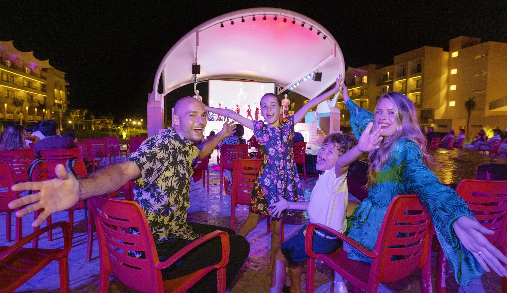 Family seated in red chairs at an outdoor night show at Planet Hollywood Cancun.