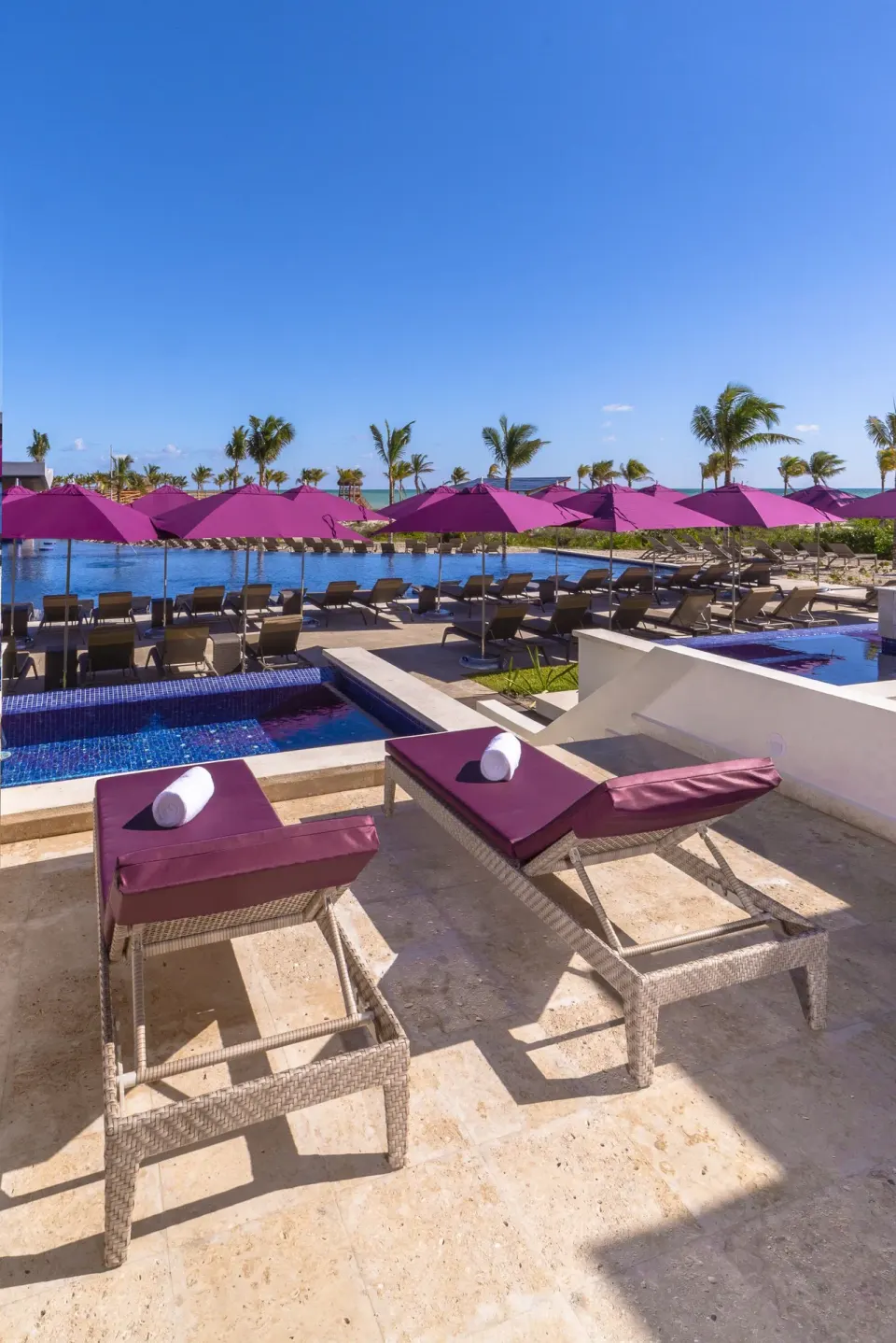 Pool loungers with purple umbrellas beside the water at Planet Hollywood Cancun.