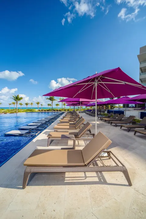 Poolside loungers and purple umbrellas beside the water at Planet Hollywood Cancun.