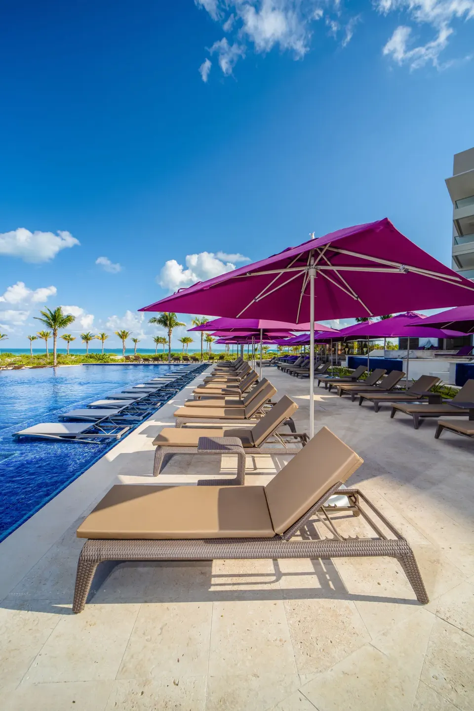 Poolside loungers and purple umbrellas beside the water at Planet Hollywood Cancun.
