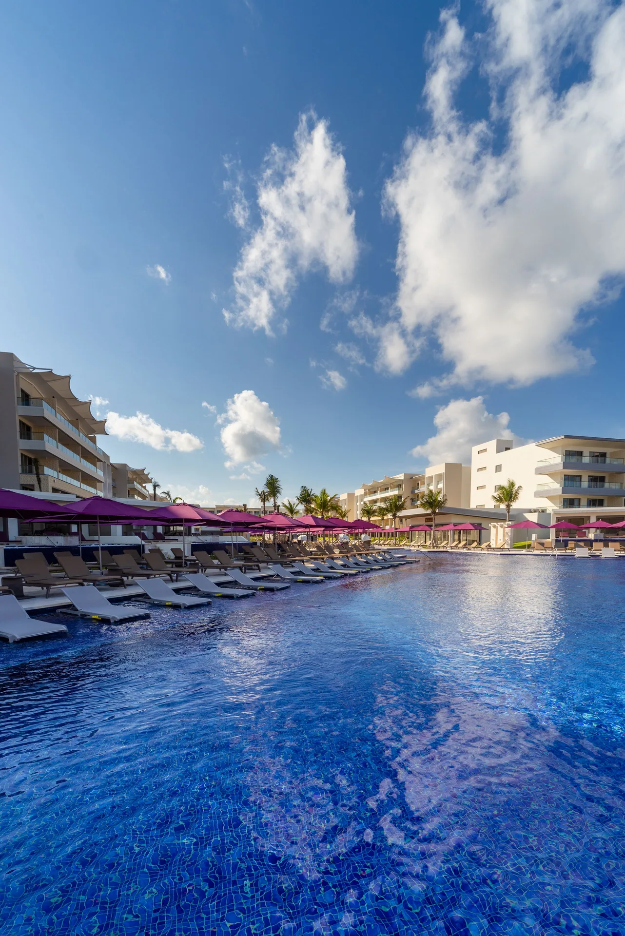 Poolside loungers and pink umbrellas along a blue pool at Planet Hollywood Cancun.
