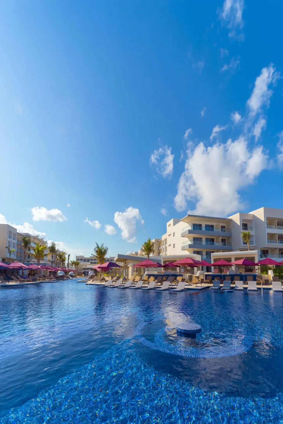 Large blue resort pool with loungers and pink umbrellas at Planet Hollywood Cancun.