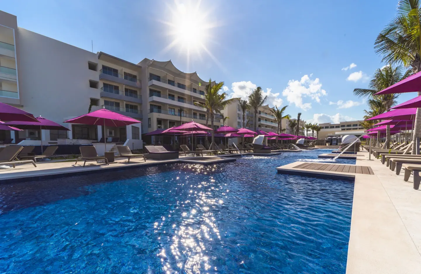 Sunny pool area with loungers, purple umbrellas, and resort buildings at Planet Hollywood Cancun.