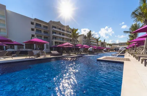 Sunny pool area with loungers, purple umbrellas, and resort buildings at Planet Hollywood Cancun.
