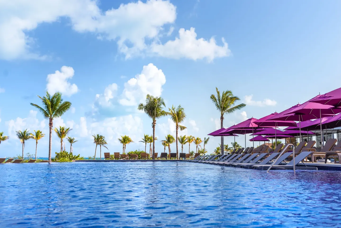 Water-level view of pool loungers, palms, and purple umbrellas at Planet Hollywood Cancun.