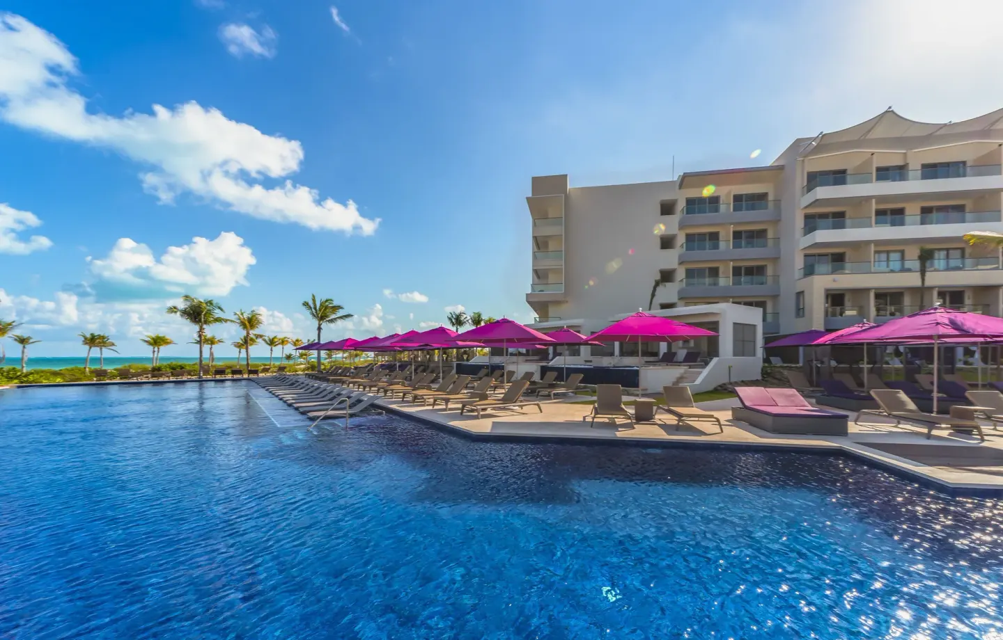 Wide pool view with loungers, purple umbrellas, and resort building at Planet Hollywood Cancun.