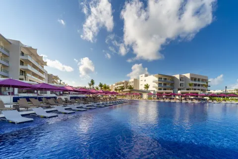 Wide resort pool bordered by loungers, pink umbrellas, and white buildings at Planet Hollywood Cancun.