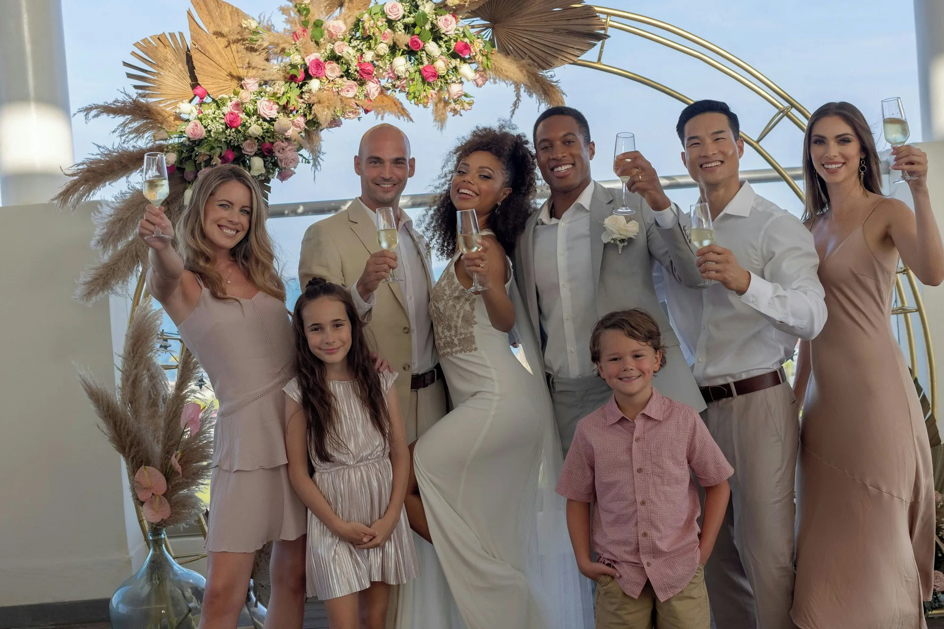 Wedding group toasts under a floral arch at Planet Hollywood Cancun.