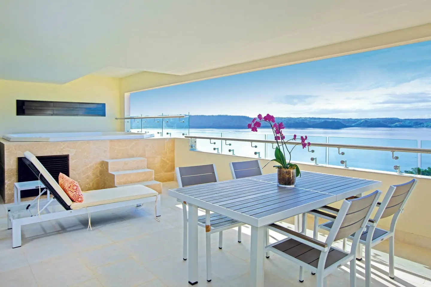 Covered terrace with dining table, lounge chair, hot tub, and bay view at Planet Hollywood Costa Rica.