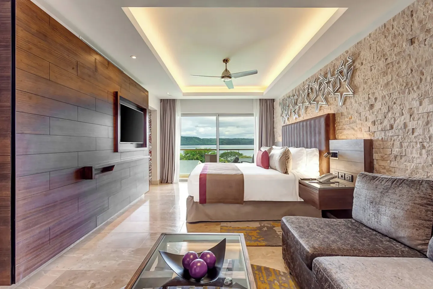 King bed suite with sofa, TV wall, and bay-facing window at Planet Hollywood Costa Rica.