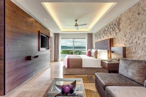 King bed suite with sofa, TV wall, and bay-facing window at Planet Hollywood Costa Rica.