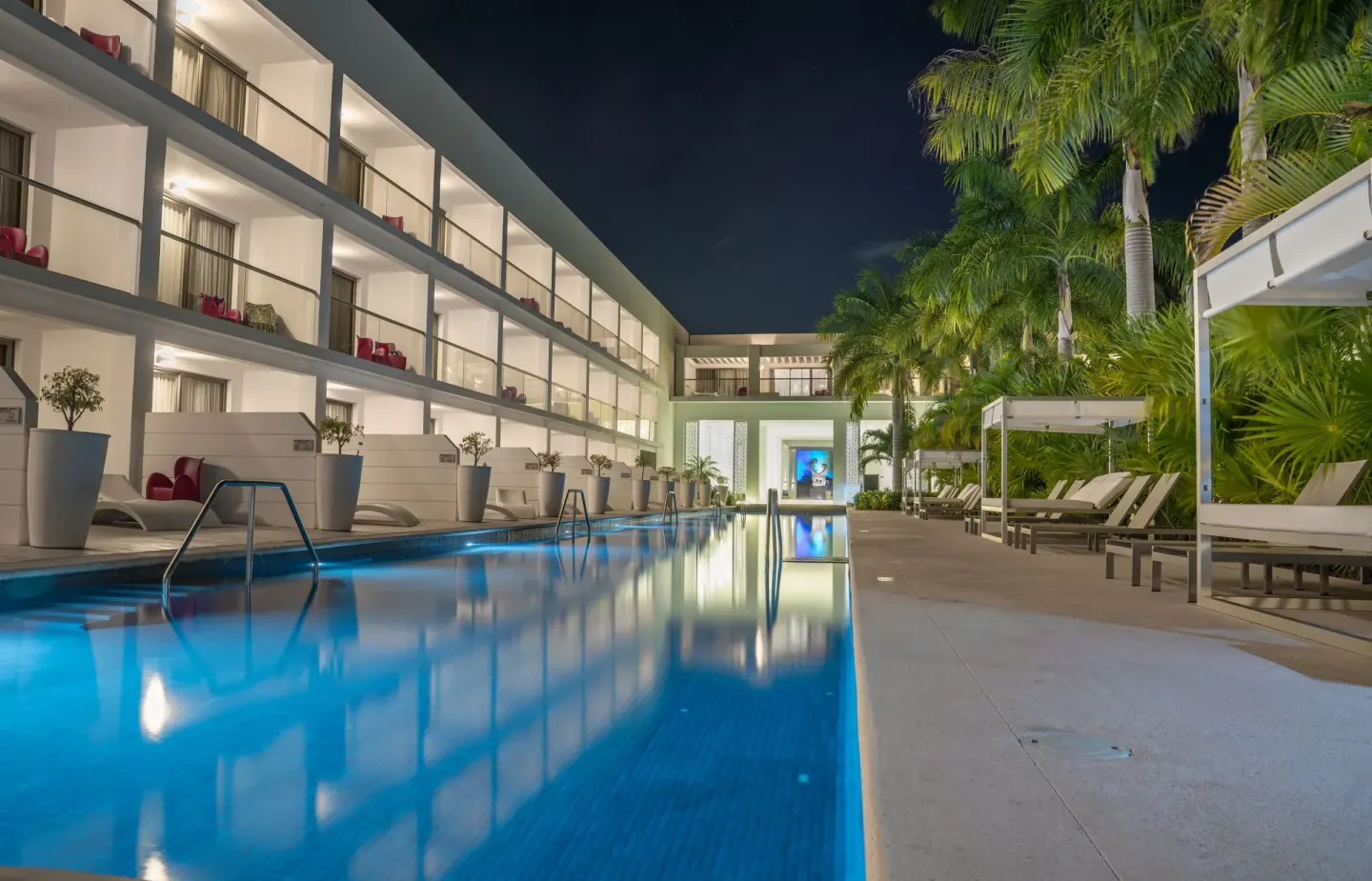 Illuminated pool corridor with palms and loungers at night at Platinum Yucatan Princess.