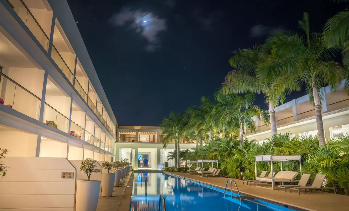 Night pool courtyard with palms, loungers, and guest room balconies at Platinum Yucatan Princess.