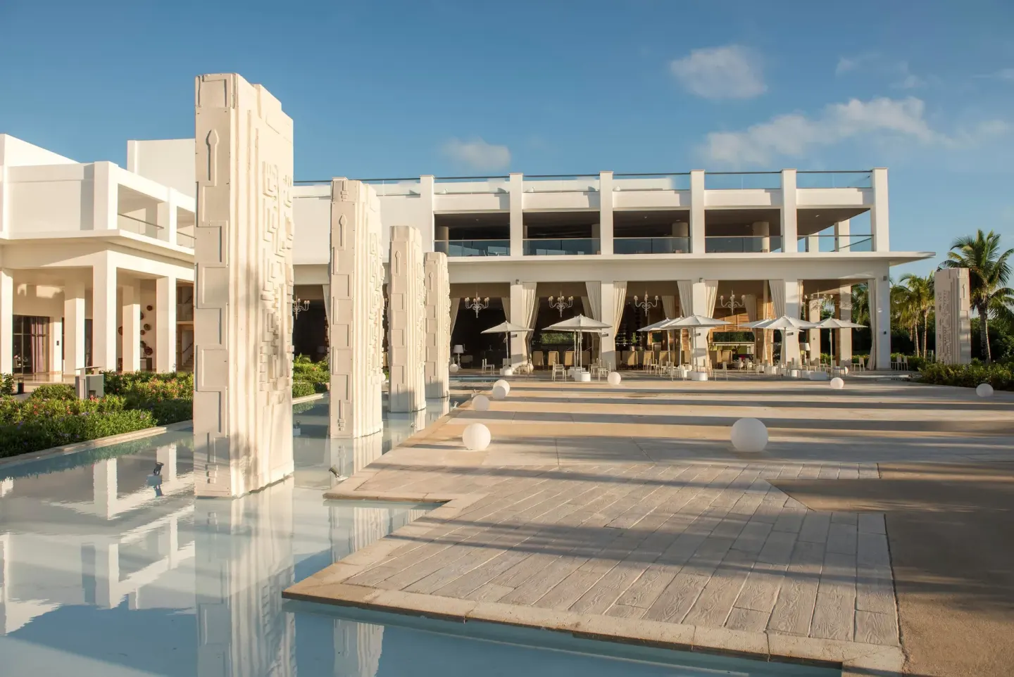Sunlit plaza with reflecting water and white resort building at Platinum Yucatan Princess.