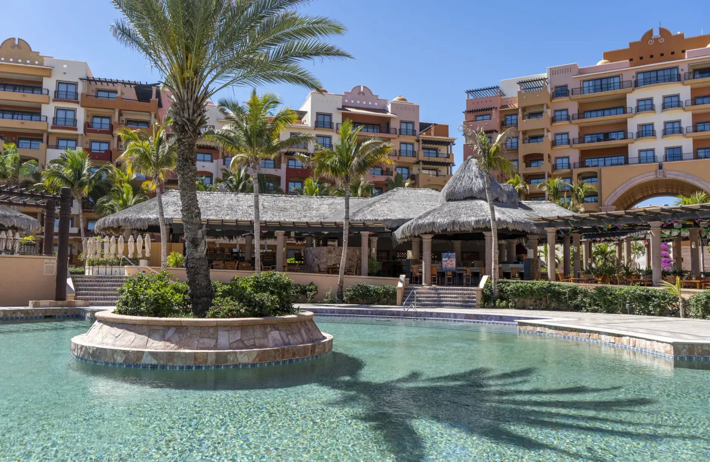 Palm island in a clear pool with resort buildings behind at Playa Grande Resort & Grand Spa.