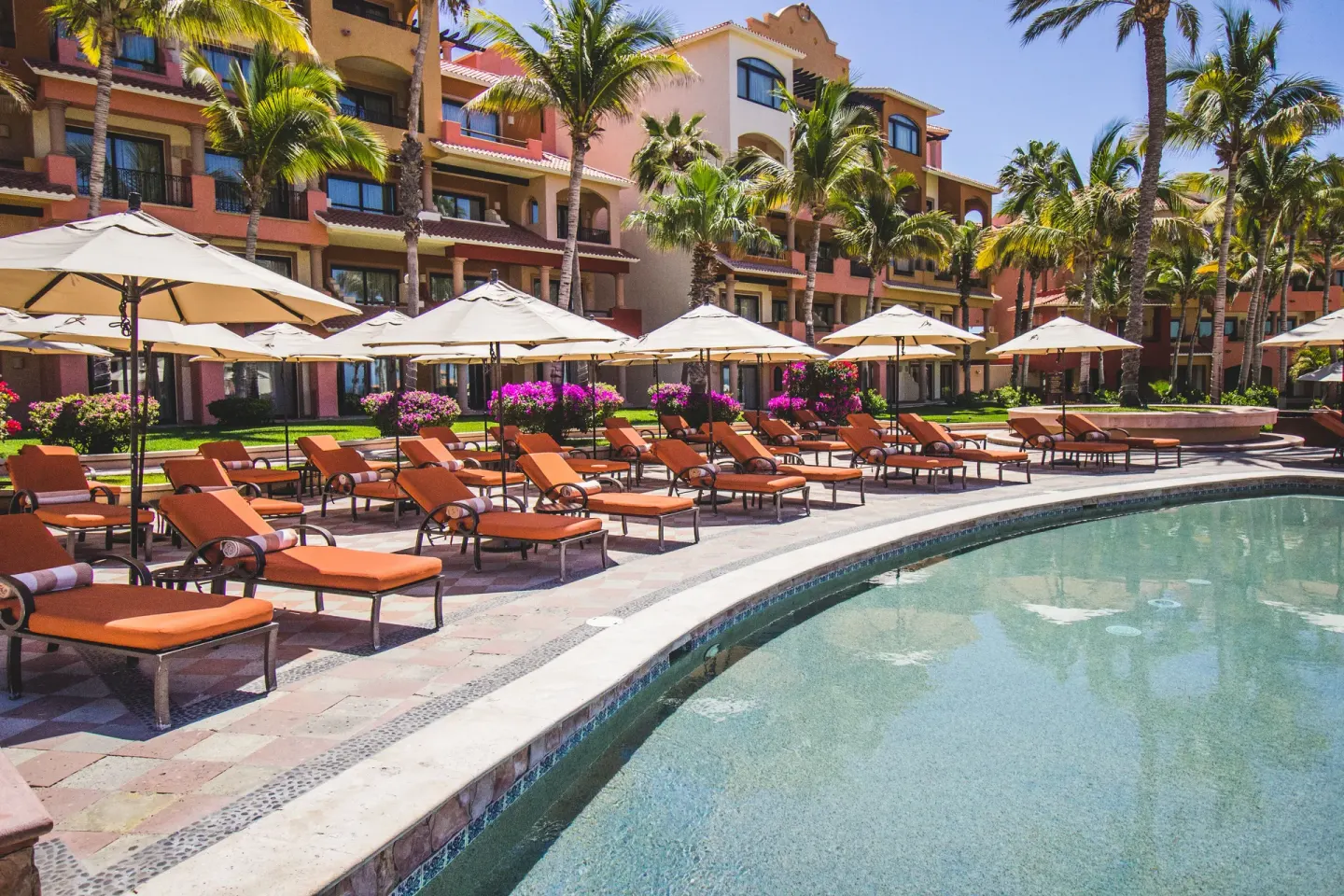 Curved pool edge with orange loungers and umbrellas at Playa Grande Resort & Grand Spa.