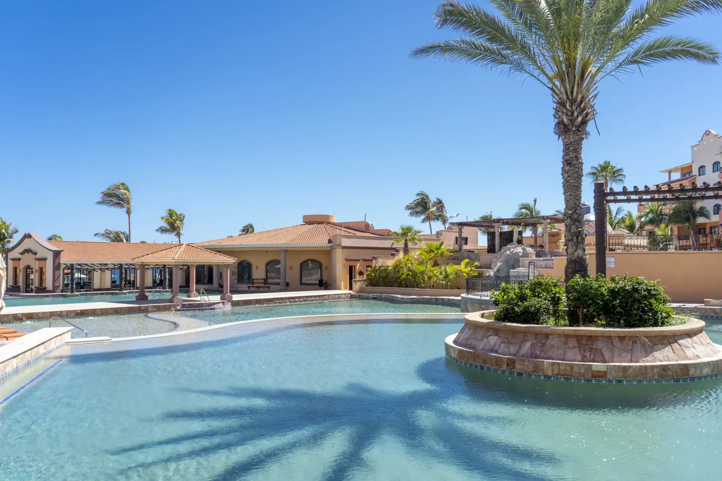 Wide resort pool with a palm planter and low buildings at Playa Grande Resort & Grand Spa.