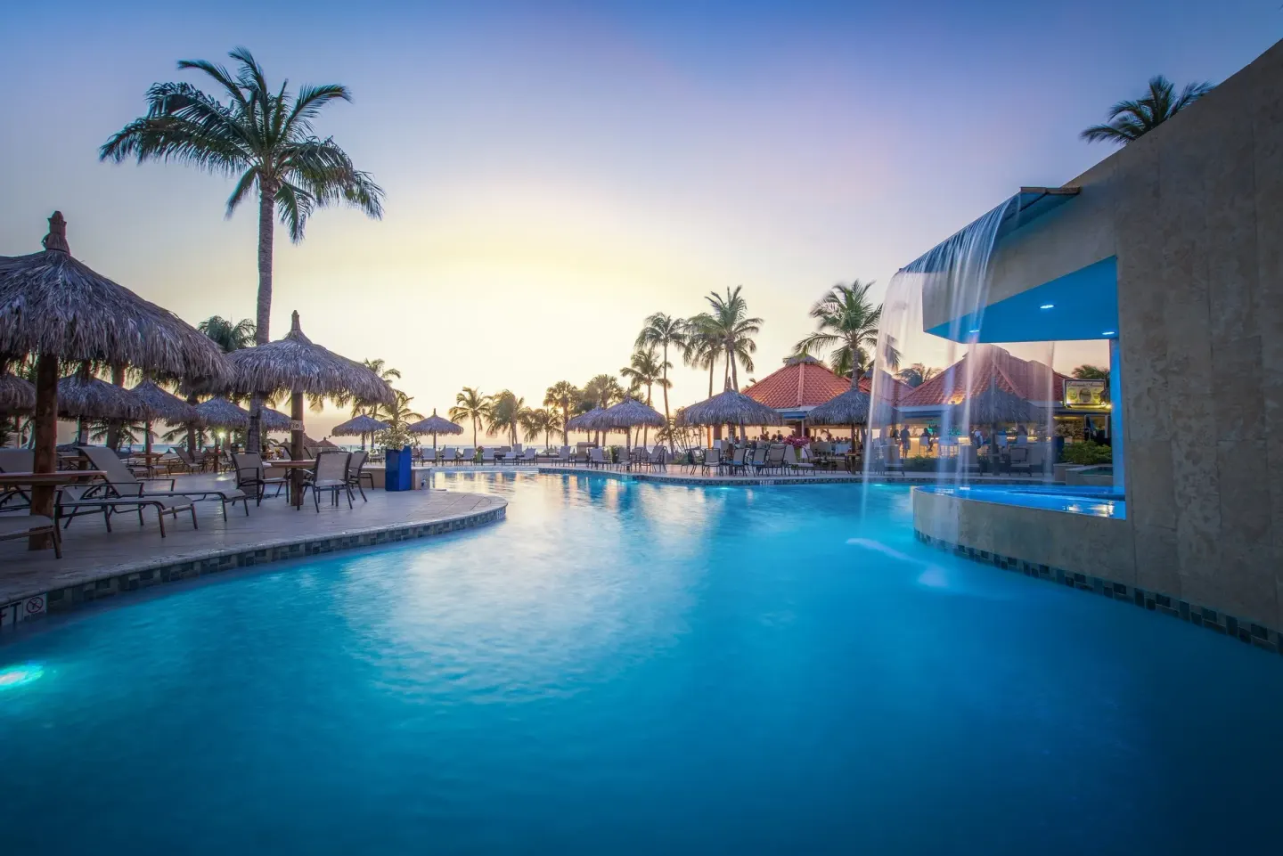 Evening pool scene with waterfall, palapas, and palm trees at Playa Linda Beach Resort.