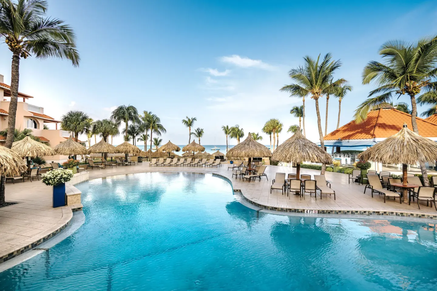 Curved pool with palapas, palms, and ocean beyond at Playa Linda Beach Resort.