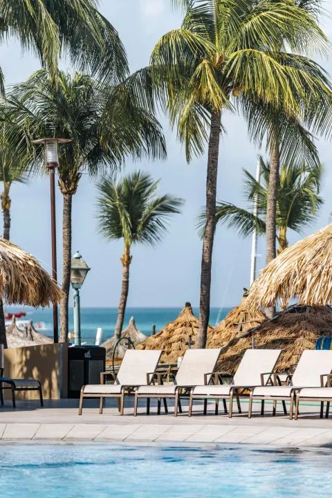 Poolside lounge chairs, palapas, palm trees, and ocean beyond at Playa Linda Beach Resort.