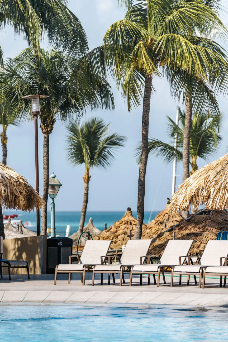 Poolside lounge chairs, palapas, palm trees, and ocean beyond at Playa Linda Beach Resort.